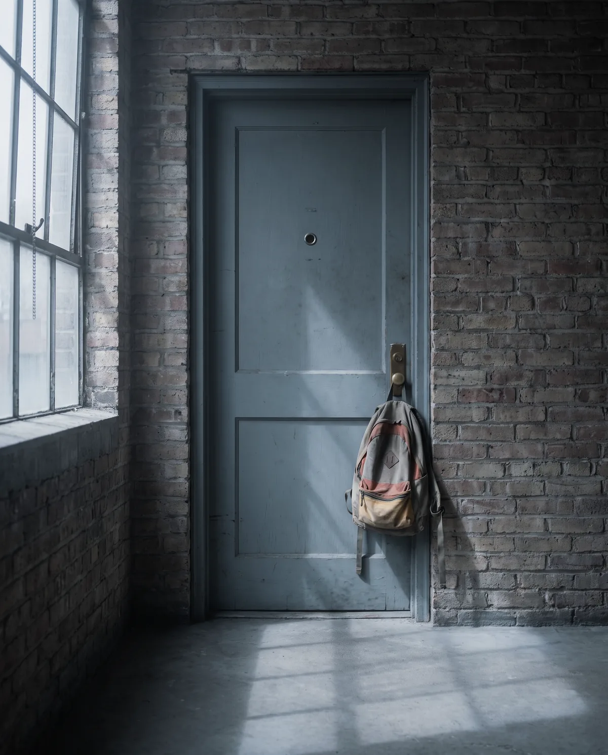 A different front door, an apartment entry, at the same morning hour, a backpack hanging on the handle.