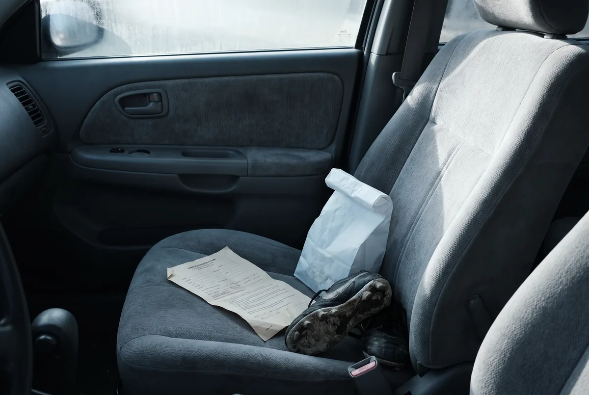 A passenger seat holding the month's paper: a camp form, a pharmacy bag and a pair of cleats.