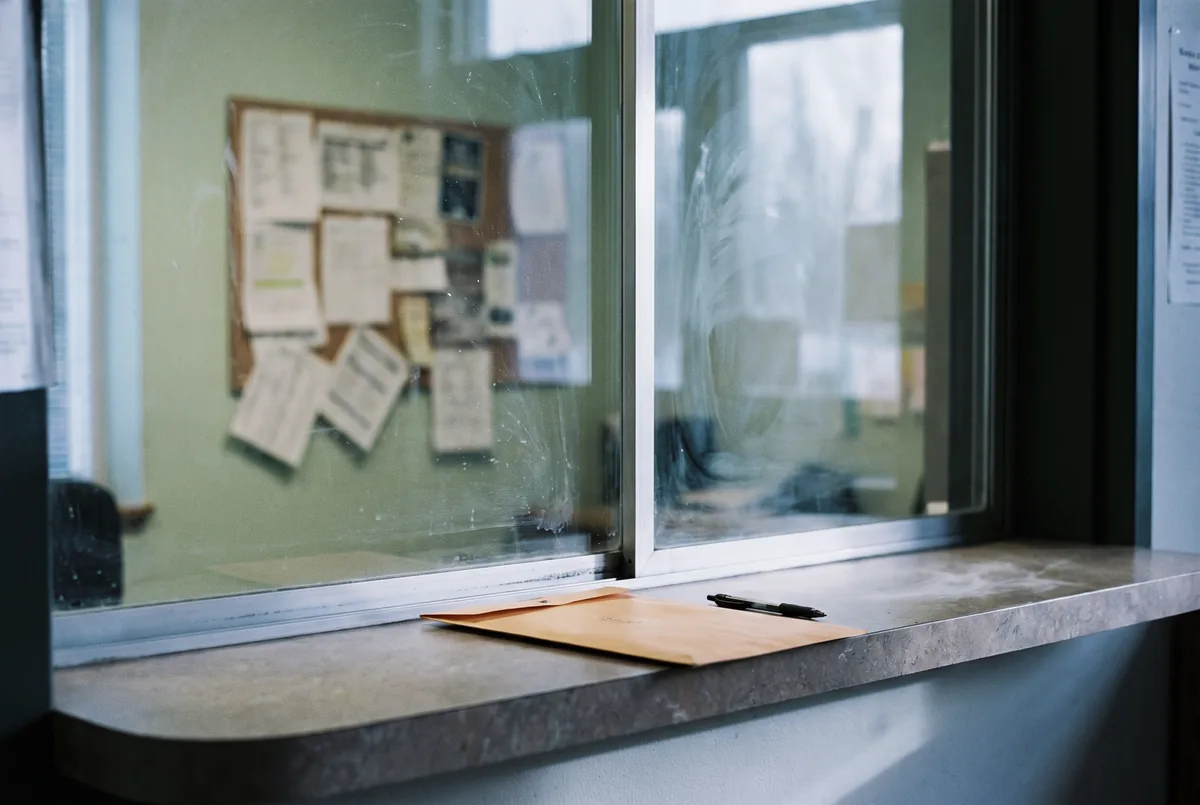A school office counter with a photo order envelope and a pen, seen from the parent's side of the window.
